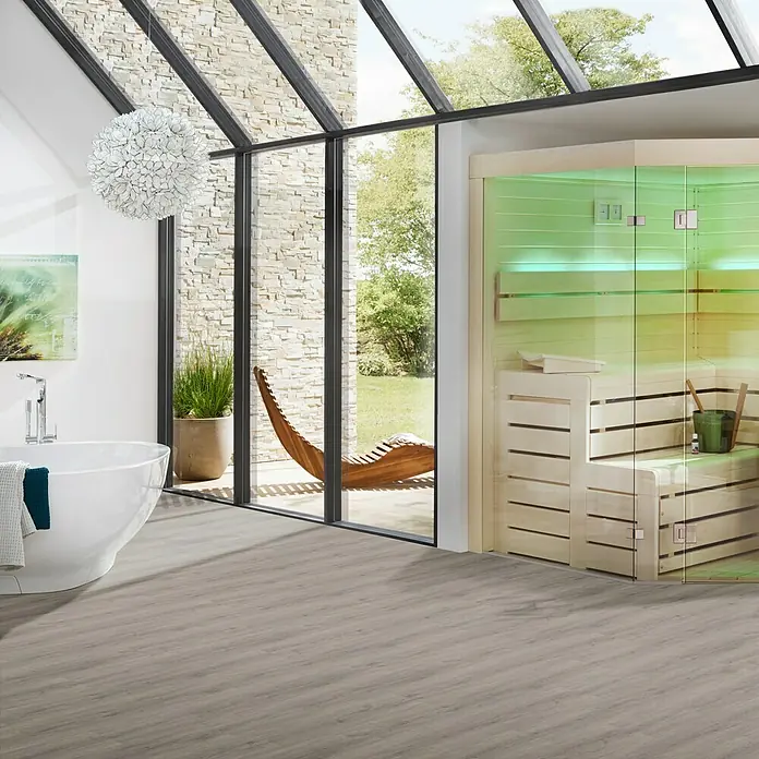 b!design Vinylboden Rigid Maxi - Woodstock Eiche, Landhausdiele, 1.220 x 228 x 4,8 mm - Helles Badezimmer mit freistehender Badewanne, Sauna und großen Fenstern, die den Blick auf den Garten freigeben. Elegantes und modernes Design.