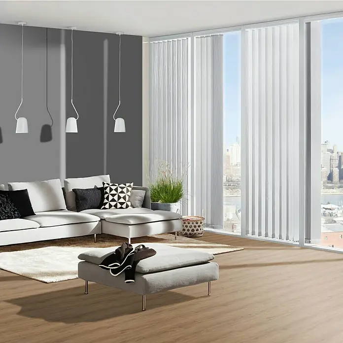 b!design Vinylboden Rigid Maxi - Columbia Eiche, Landhausdiele, 1.220 x 228 x 4,8 mm - Das Bild zeigt eine moderne Wohnzimmereinrichtung mit einer eleganten grauen Couch, einem passenden Hocker und weißen Vertikaljalousien.
