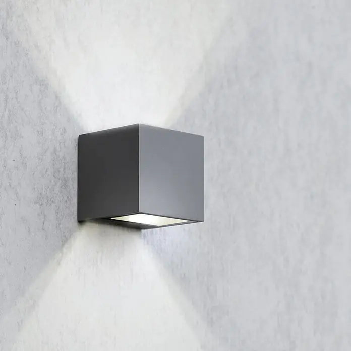 Lutec Aplique exterior LED Gemini - 9 W, 88 x 85 x 86 mm, Antracita, IP54 - Moderna lámpara de pared cúbica gris con haces de luz, montada en una pared blanca, que proporciona una solución de iluminación exterior elegante.