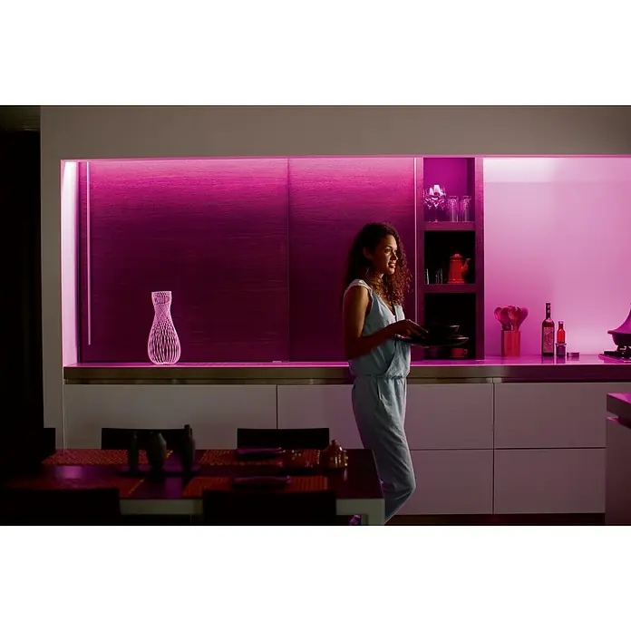 Philips Hue LED-Band Plus Erweiterung - 1 m, RGBW - Frau in moderner Küche mit Philips Hue Beleuchtung, die Ambiente schafft. Perfekt für gemütliche Abende mit stimmungsvollem Licht.