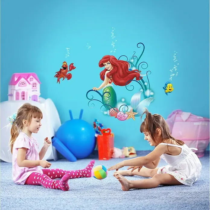 Komar Disney Edition 4 Dekosticker Arielle - 8 -tlg., Bunt - Kinderzimmer mit Wandtattoo "Arielle die Meerjungfrau", zwei Mädchen spielen mit einem bunten Ball auf einem blauen Teppich.