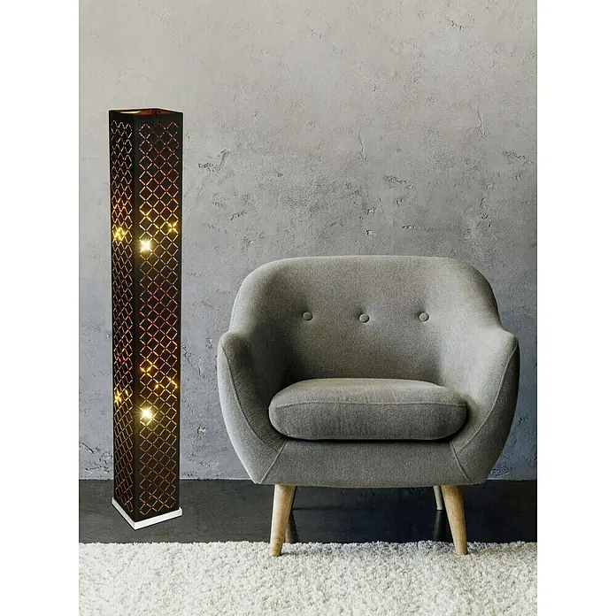Tween Light Stehleuchte - Höhe: 118 cm - Dekorative Stehlampe mit einem geometrischen Muster und warmem Licht, die neben einem grauen Sessel auf einem Teppich steht.