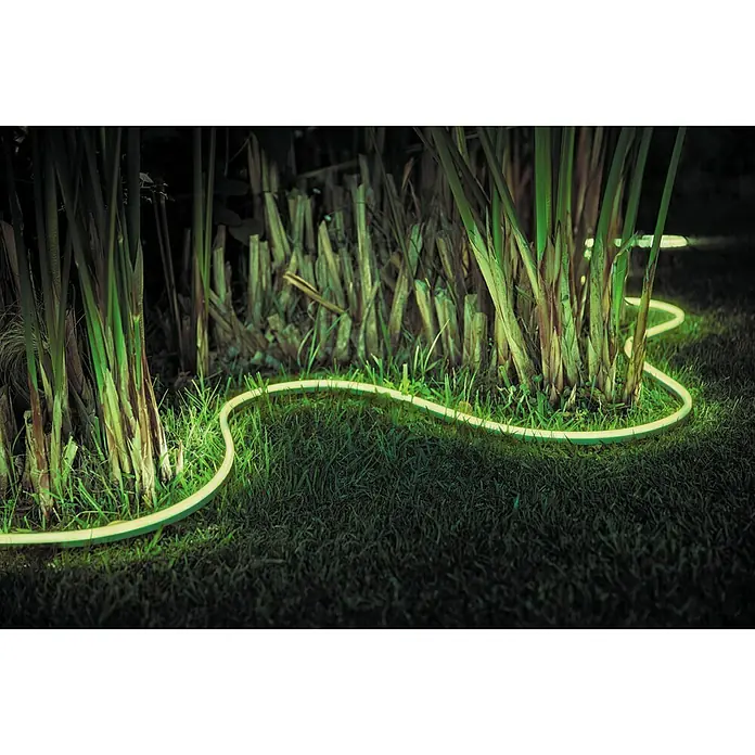 Philips Hue LED-Band Outdoor - Länge: 2 m, Lichtfarbe: RGBW, 19 W, 780 lm - Eine grüne LED-Lichterkette schlängelt sich durch einen Garten, um Pflanzen herum und erhellt die Nacht.