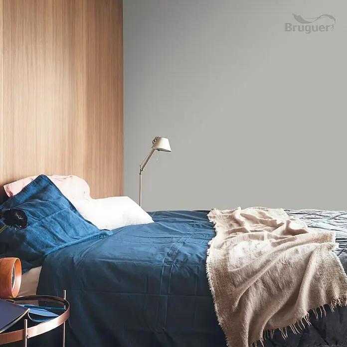 Bruguer Colores del Mundo Tester de pintura - Patagonia perla intermedio, Mate, 30 ml - Dormitorio con cama doble, ropa de cama azul y manta beige frente a una pared gris. Logotipo de la marca "Bruguer" en la esquina.