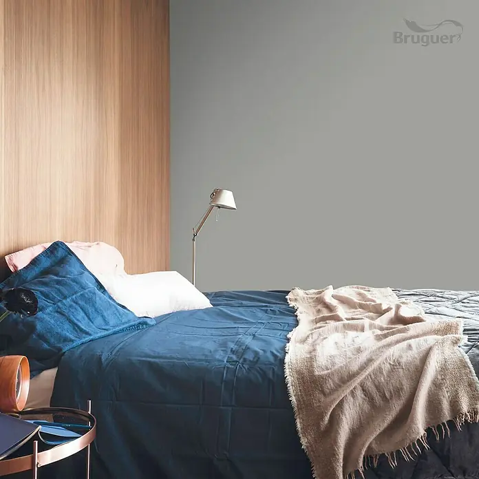 Bruguer Colores del Mundo Tester de pintura - Patagonia perla natural, Mate, 30 ml - Acogedora habitación con ropa de cama azul y una pared pintada de gris. La marca Bruguer es visible en la imagen.