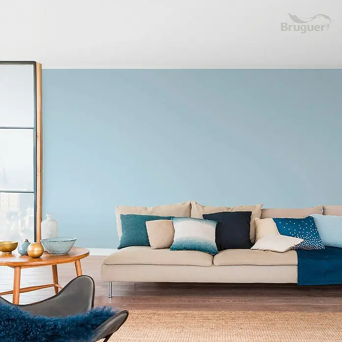 Bruguer Colores del Mundo Tester de pintura - Mediterráneo azul intermedio, Mate, 30 ml - Salón con pintura de pared azul claro de Bruguer, sofá con cojines y mesa de madera. Ambiente acogedor y atractivo.