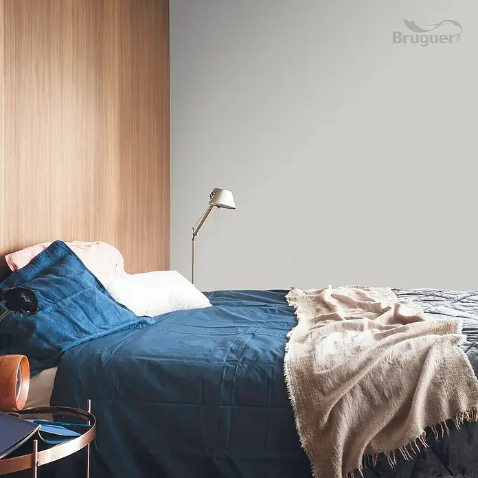 Bruguer Colores del Mundo Tester de pintura - Patagonia perla suave, Mate, 30 ml - Dormitorio con cama, ropa de cama azul, paredes grises claras y detalles de madera. La pintura de pared de la marca Bruguer es un punto focal.