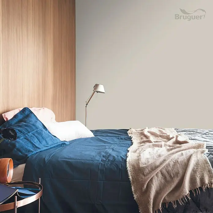 Bruguer Colores del Mundo Tester de pintura - Nepal beige intermedio, Mate, 30 ml - Dormitorio con cama azul, almohadas claras y manta beige. Diseño minimalista con tonos cálidos de madera al fondo. Iluminación suave y relajante.