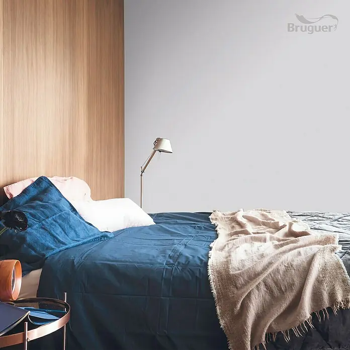 Bruguer Colores del Mundo Tester de pintura - Japón matiz de violeta, Mate, 30 ml - Dormitorio con ropa de cama azul, una mesa de noche y una lámpara frente a una pared gris.