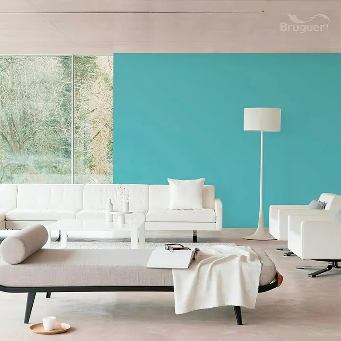 Bruguer Ultra Resist Tester de pintura - Azul turquesa, Mate, 30 ml - Salón luminoso con sofá blanco, sillones y pared de acento turquesa. Una manta blanca está sobre la otomana gris.