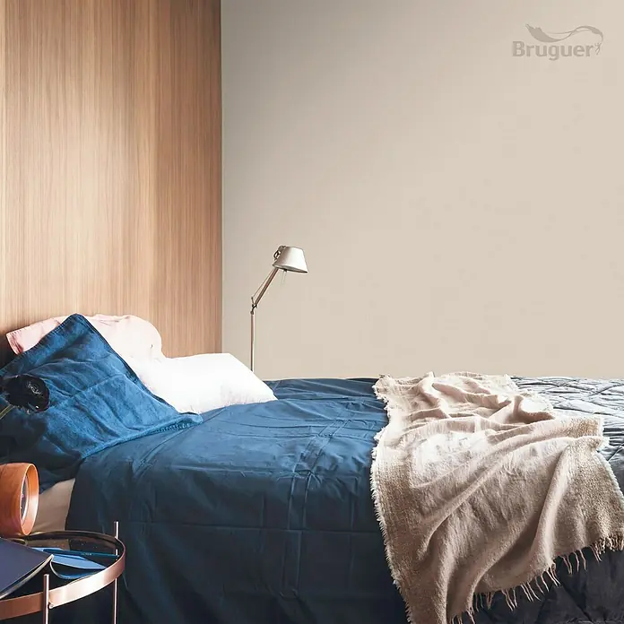 Bruguer Colores del Mundo Tester de pintura - Kenia marrón suave, Mate, 30 ml - Un dormitorio con una cama acogedora con ropa de cama azul, almohadas y una manta suave. La pared está pintada en un tono beige cálido.