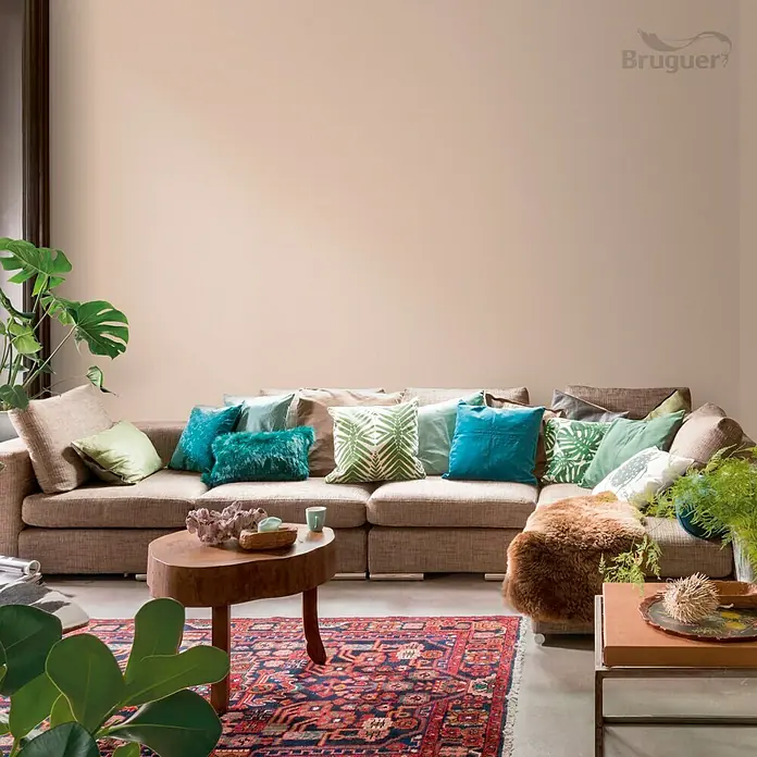Bruguer Colores del Mundo Tester de pintura - Kenia marrón intermedio, Mate, 30 ml - Salón con sofá beige, cojines coloridos y mesa de madera. La pared está pintada en un suave tono melocotón.