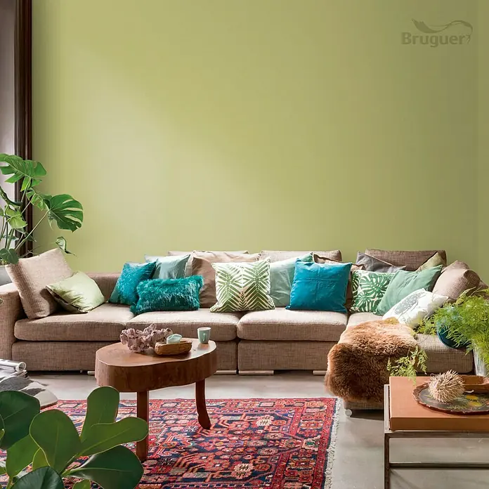 Bruguer Colores del Mundo Tester de pintura - Amazonas verde natural, Mate, 30 ml - Salón con un sofá acogedor con cojines, una mesa redonda de madera, todo complementado perfectamente por la pintura de pared de Bruguer.