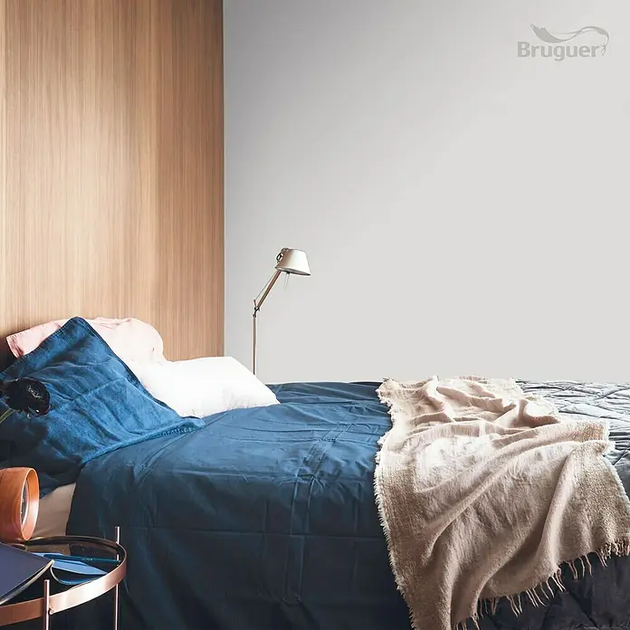 Bruguer Colores del Mundo Tester de pintura - Kenia matiz de marrón, Mate, 30 ml - Dormitorio con ropa de cama azul, pared de madera y una lámpara, con la pared pintada en un tono claro de Bruguer.