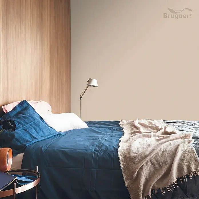 Bruguer Colores del Mundo Tester de pintura - Kenia marrón intermedio, Mate, 30 ml - Dormitorio con cama doble, ropa de cama azul y una manta clara, y una lámpara. La pared está pintada en un tono claro.