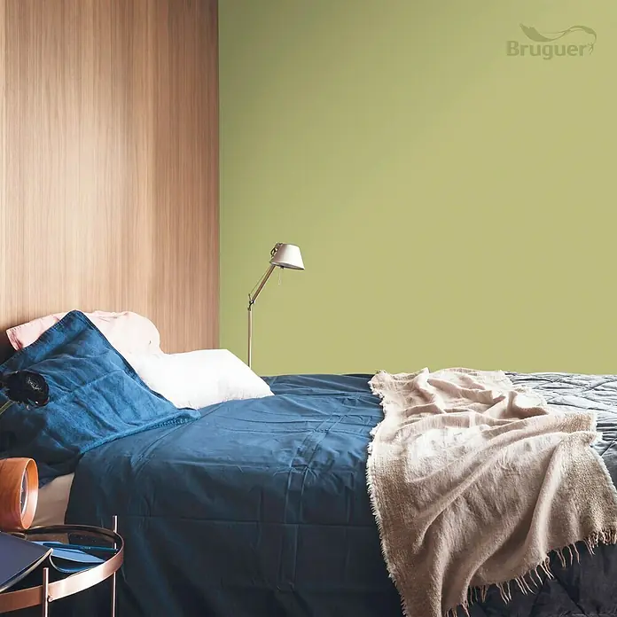 Bruguer Colores del Mundo Tester de pintura - Amazonas verde natural, Mate, 30 ml - Un dormitorio con una pared de acento verde y una cama de madera adornada con un edredón azul y almohadas.