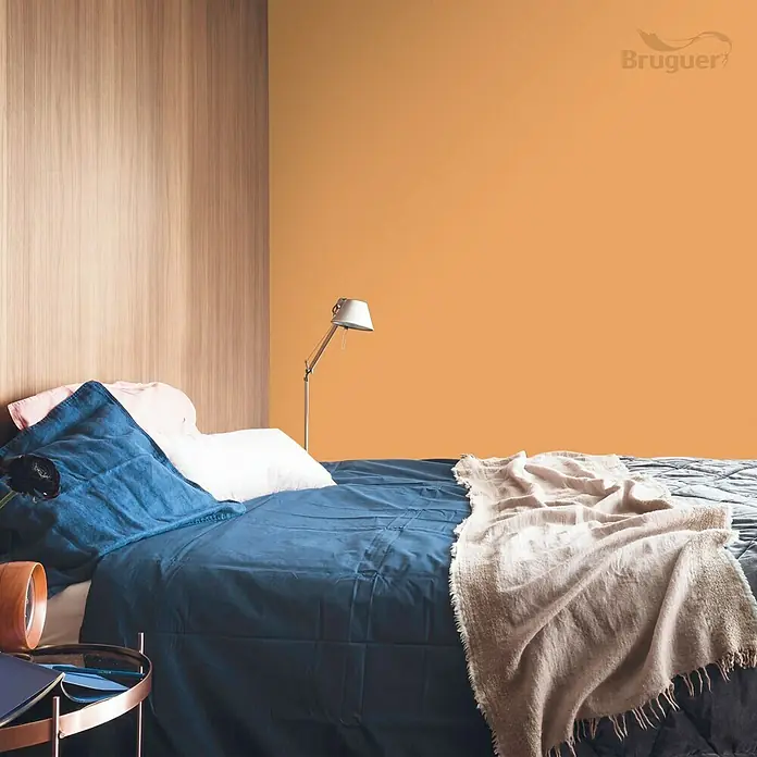 Bruguer Colores del Mundo Tester de pintura - India melocotón natural, Mate, 30 ml - Un dormitorio con una pared pintada de naranja y una cama cubierta con ropa de cama azul. La pintura de la pared es de la marca Bruguer.
