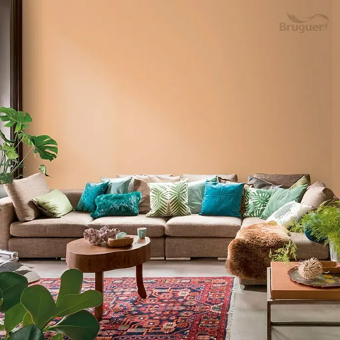 Bruguer Colores del Mundo Tester de pintura - Egipto ocre natural, Mate, 30 ml - Salón con un gran sofá, muchos cojines y una pequeña mesa de madera, pintado en un tono cálido y acogedor.