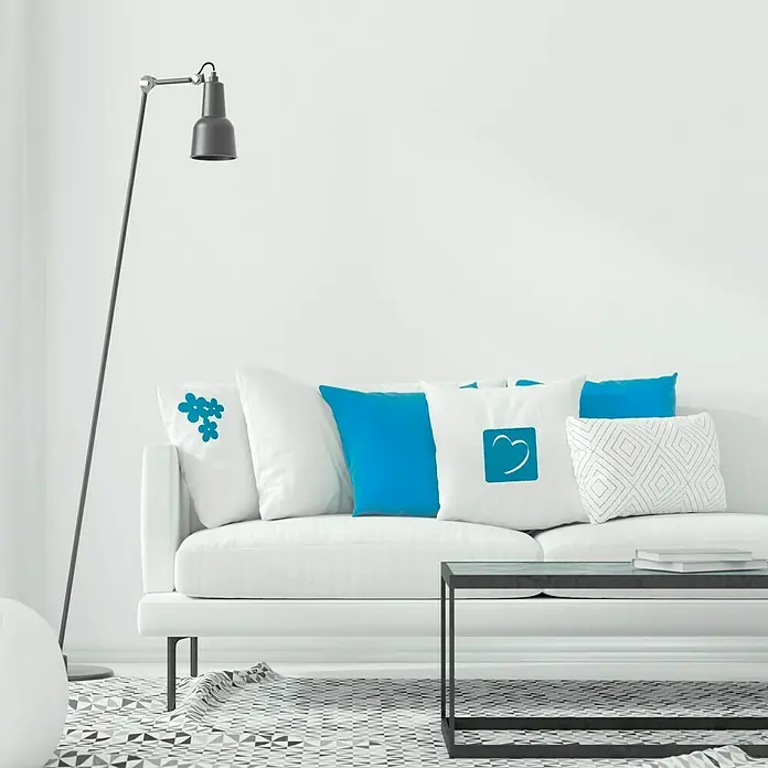 Vinilo de pared Corazón - Turquesa, Textil - Un sofá blanco adornado con cojines azules y blancos, con un patrón floral, un corazón y formas geométricas.