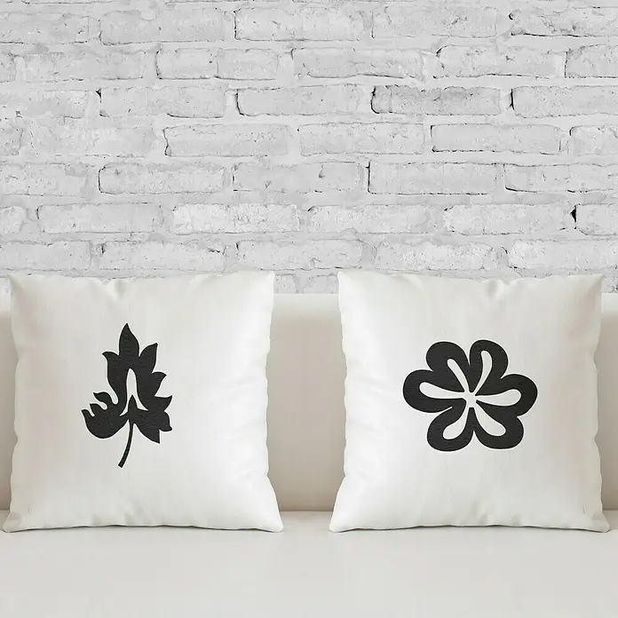 Vinilo de pared Flor - 27 x 23 cm, Negro, Textil - Dos cojines blancos con diseños florales estilizados sobre un fondo de pared de ladrillo blanco.