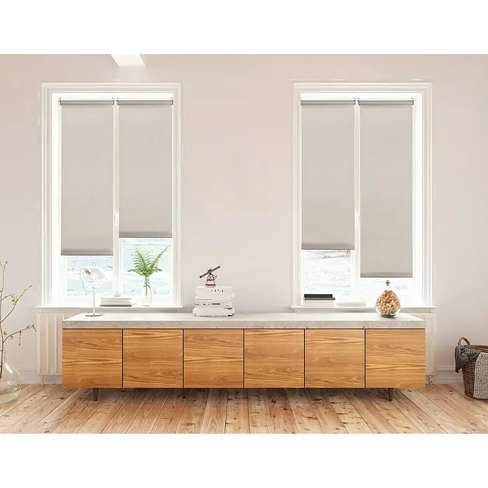 Estor enrollable Clip&Fix - An x Al: 45 x 180 cm, Piedra - Un salón moderno con dos ventanas cubiertas con persianas enrollables grises, que proporcionan una decoración de ventana elegante y funcional.