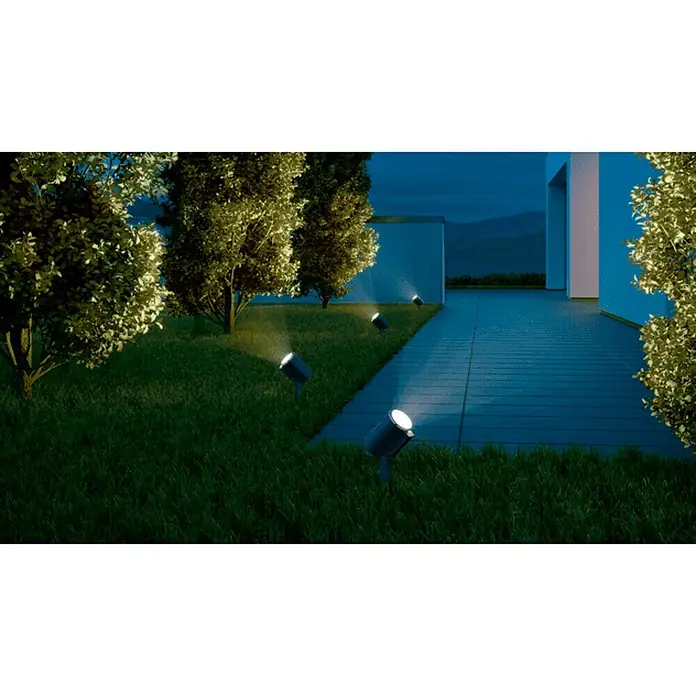 Steinel Lámpara de pie para exterior Spot Garden N - 7,86 W, Color del marco: Antracita, Blanco cálido, 14 x 6,9 x 36,9 cm - Una acogedora escena de jardín con varios focos exteriores que iluminan árboles y caminos, creando un ambiente cálido.