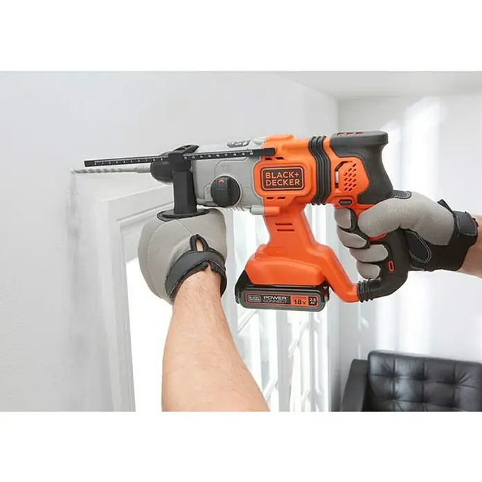 Black+Decker Martillo combinado de batería BCD900E2K - 18 V, 2 baterías, 1,2 J - Un martillo perforador inalámbrico Black+Decker está siendo utilizado para perforar un agujero en una pared. El martillo perforador es naranja y negro.