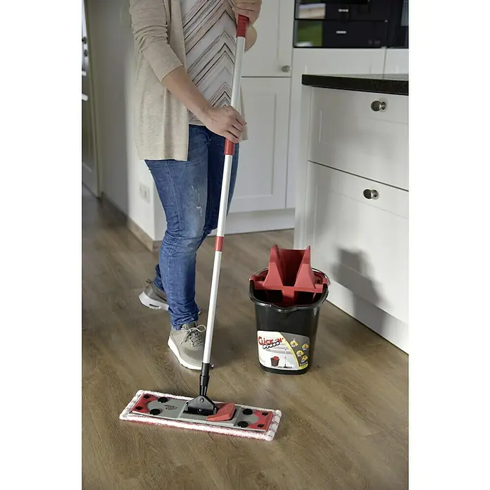 Sprintus Bodenwisch-Set Click N Press + Staubmop - 12 l, 5 -tlg., Materialzusammensetzung Bezug: 80 % Mikrofaser, 20 % weiche Abrasivborsten - Eine Person wischt mit einem "Click'n'Press"-Flachwischmop mit Eimer auf einem Holzboden in einer Küche.