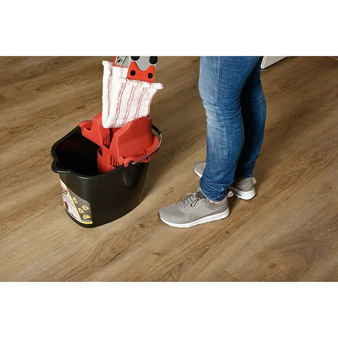 Sprintus Bodenwisch-Set Click N Press + Staubmop - 12 l, 5 -tlg., Materialzusammensetzung Bezug: 80 % Mikrofaser, 20 % weiche Abrasivborsten - Mop und Eimer stehen auf einem Holzboden neben einer Person in Jeans und Turnschuhen. Der Mop mit Stoffaufsatz steckt im Auswringer des Eimers.
