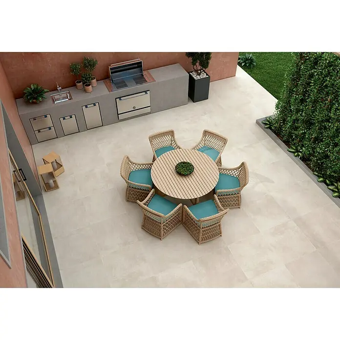 Pavimento porcelánico Rodano - 75 x 75 cm, Tiza, Rectificado, C-3 Antideslizante - Atractiva zona al aire libre con una mesa redonda de madera y seis sillas de mimbre con cojines azules, complementada con una moderna cocina exterior.