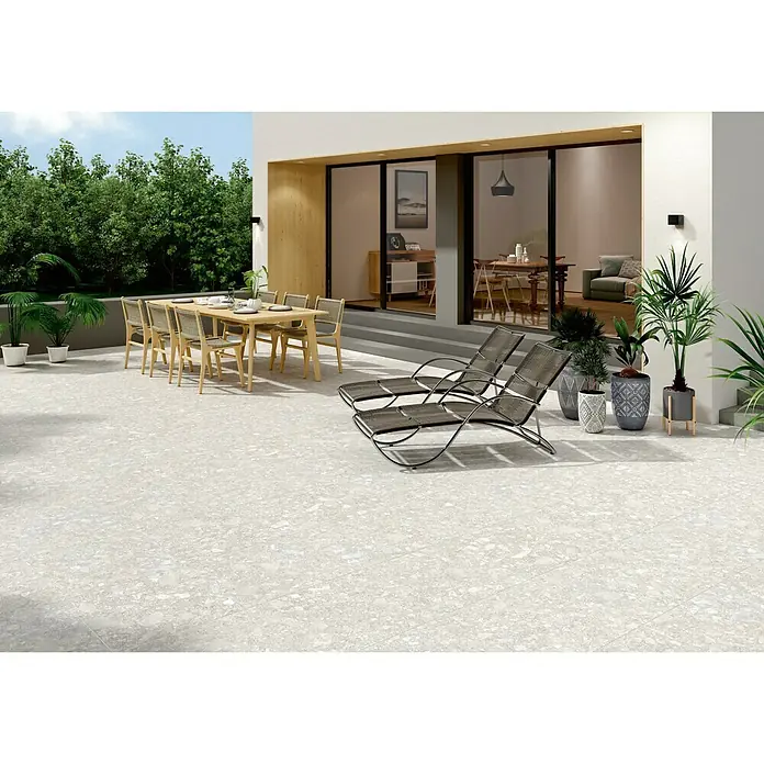 BHS Showroom Pavimento porcelánico Ceppo - 60 x 60 cm, Gris claro, Rectificado - Imagen de un área exterior con baldosas de color gris claro, muebles de jardín y plantas. Las baldosas dan un toque elegante al patio.