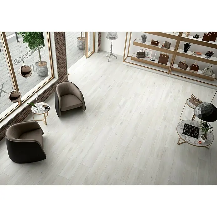 BHS Showroom Pavimento porcelánico Sanford Soft - 150 x 30 cm, Blanco, Rectificado - Baldosas de suelo claras con aspecto de madera en una elegante sala de exposición. Las baldosas crean un ambiente moderno y acogedor.
