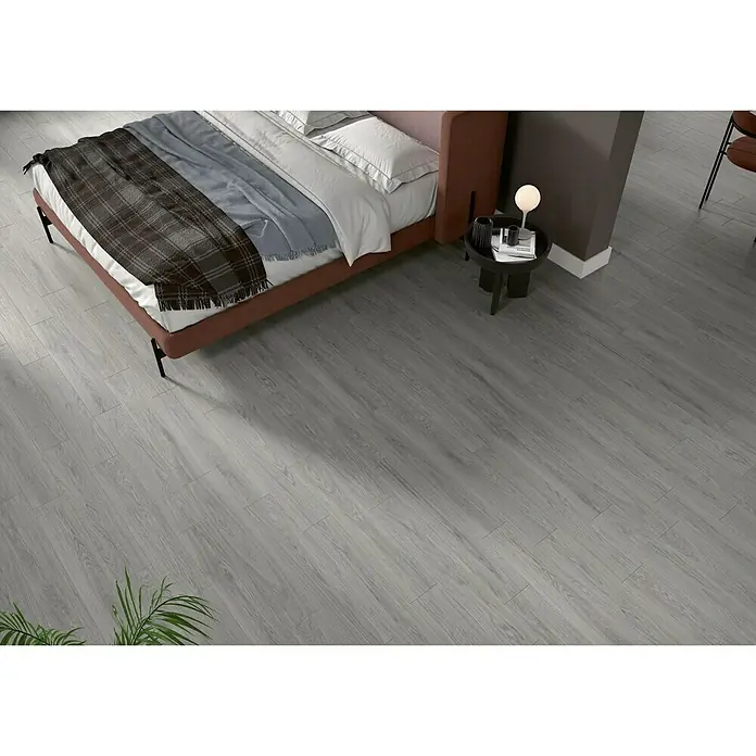 BHS Showroom Pavimento porcelánico Ninsba - 90 x 15 cm, Gris, Rectificado - Acogedora habitación con suelo de madera gris, creando un ambiente moderno y elegante. La cama y la mesita de noche complementan perfectamente el aspecto.
