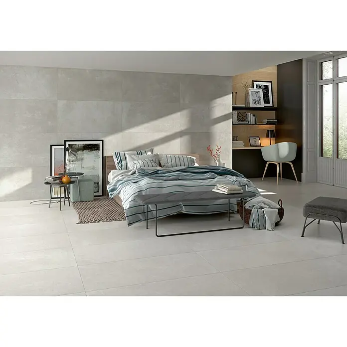 BHS Showroom Pavimento porcelánico Rodano - 120 x 60 cm, Gris claro, Rectificado - Un dormitorio luminoso con baldosas grises, una cama con ropa de cama a rayas azules y blancas, y una pequeña zona de escritorio al fondo.