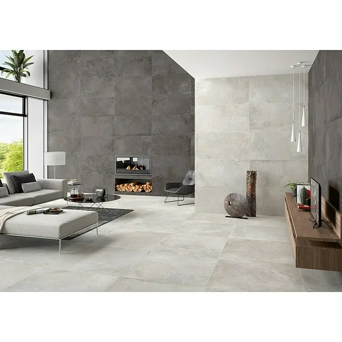 BHS Showroom Pavimento porcelánico Lorraine - 120 x 60 cm, Gris oscuro, Rectificado - Un salón moderno con grandes baldosas de color gris claro en el suelo, pared gris con chimenea y sofá de color claro.