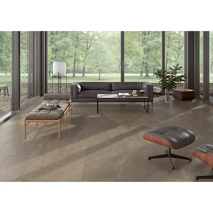 BHS Showroom Pavimento porcelánico Talo - 75 x 75 cm, Natural, Rectificado - Elegante sala de estar con baldosas grises, sofá, tumbona y sillón, con vistas a la naturaleza por la ventana.