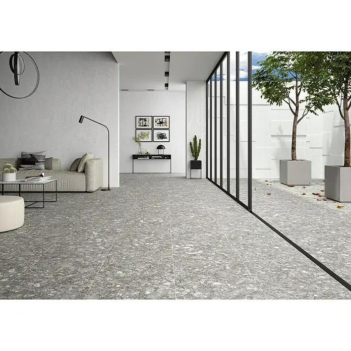 BHS Showroom Pavimento porcelánico Ceppo - 60 x 60 cm, Gris oscuro, Rectificado - Una amplia estancia con suelo de baldosas tipo terrazo, que se extiende desde una zona de estar hasta un espacio exterior acristalado.