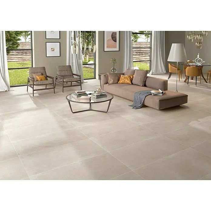 BHS Showroom Pavimento porcelánico Claire - 120 x 60 cm, Taupe, Rectificado - Vista interior de una sala de estar con baldosas de piso beige, sofá, sillones, mesa de centro, lámparas y ventanas con vistas a zonas verdes.