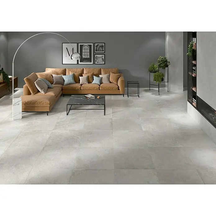 BHS Showroom Pavimento porcelánico Lorraine - 60 x 60 cm, Gris, Rectificado - Una sala de estar con baldosas grises que ofrece un ambiente elegante y moderno, complementado con un sofá seccional cómodo.