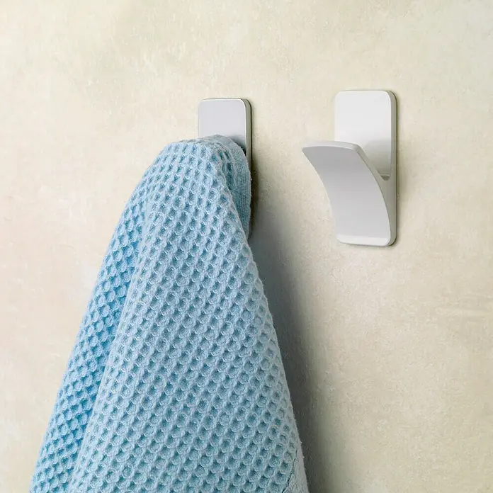 Inofix Colgador adhesivo 2191 - L x An x Al: 30 x 25 x 60 mm, Plástico, Blanco - Toalla colgada de dos ganchos blancos en una pared beige. Los ganchos tienen un diseño minimalista y la toalla azul es suave y absorbente.