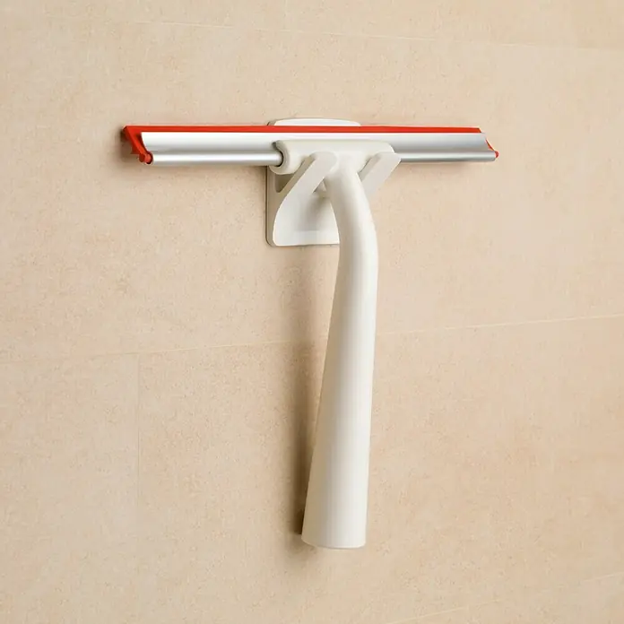 Inofix Colgador adhesivo 2192 - Blanco - Un limpiacristales de ducha con labio rojo y mango blanco cuelga en un azulejo de pared de color claro, listo para usar en el baño.