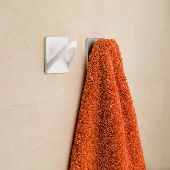 Inofix Colgador adhesivo 2190 - L x An x Al: 65 x 45 x 65 mm, Plástico, Blanco - Toalla colgada en un gancho de pared en el baño. La toalla esponjosa, de color naranja, llama la atención en la pared luminosa.