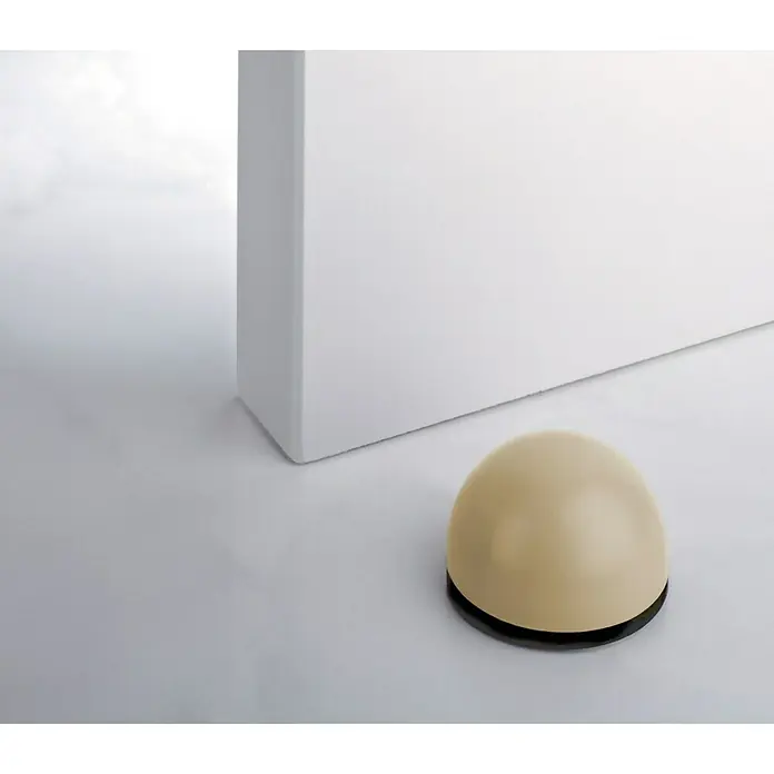 Inofix Tope de puerta 2033 - Beige, Plástico, 6 ud. - Un tope de puerta de color crema con base negra se encuentra junto a un objeto blanco sobre una superficie blanca.
