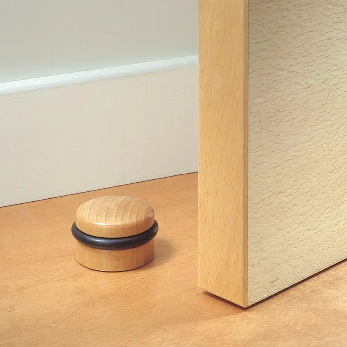Inofix Tope de puerta 2032 - Madera, Haya, 6 ud. - Un tope de puerta de madera con un anillo de goma negra se encuentra en un piso de madera junto a una puerta. Accesorio práctico.