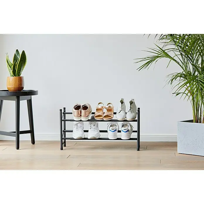 Schuhregal Loft - L x B x H: 23 x 116 x 36 cm, Schwarz - Schuhregal aus Metall mit zwei Ebenen mit verschiedenen Schuhen, neben einem Hocker mit einer Pflanze und einer größeren Pflanze.