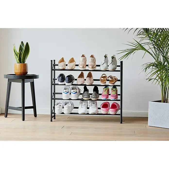 Schuhregal Loft - L x B x H: 23 x 116 x 68 cm, Schwarz - Ein schwarzes Schuhregal mit verschiedenen Schuhen, neben einem Hocker mit einer Pflanze und einer großen Grünpflanze.