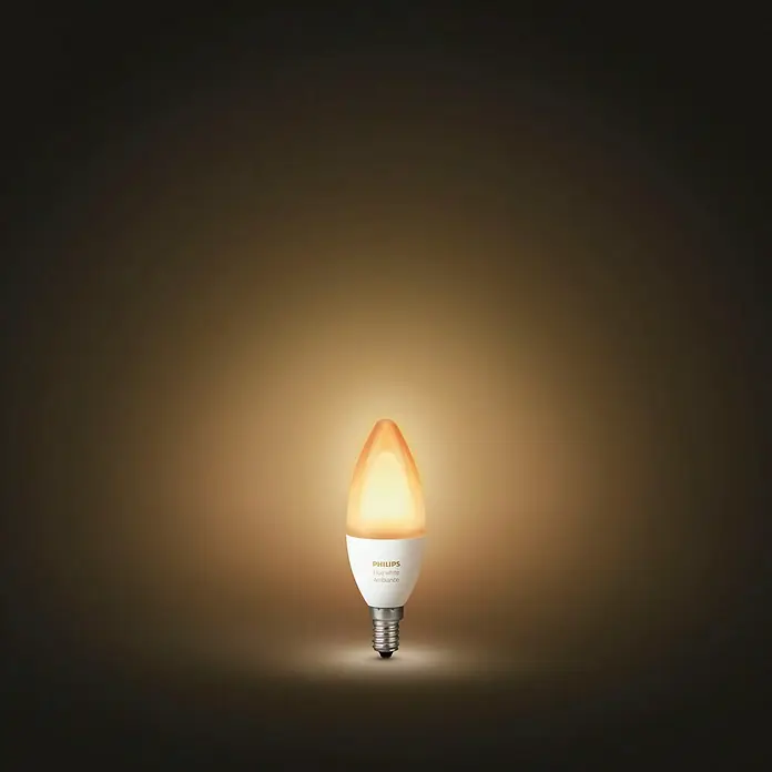 Philips Hue Smart-LED-Lampe White Ambiance - E14, Dimmbar, Warmweiß, 470 lm, 5,2 W - Nahaufnahme einer Philips Hue White Ambiance Kerzenlampe, die warmes Licht ausstrahlt, vor einem dunklen Hintergrund.