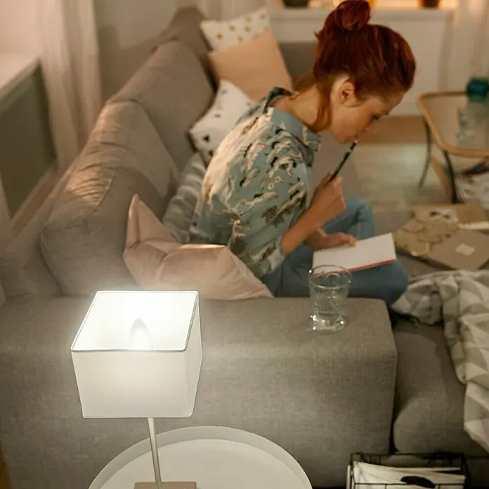Philips Hue Smart-LED-Lampe White Ambiance - E14, Dimmbar, Warmweiß, 470 lm, 5,2 W - Das Bild zeigt eine moderne Nachttischlampe mit einem quadratischen, weißen Lampenschirm, die ein warmes, gemütliches Licht spendet.
