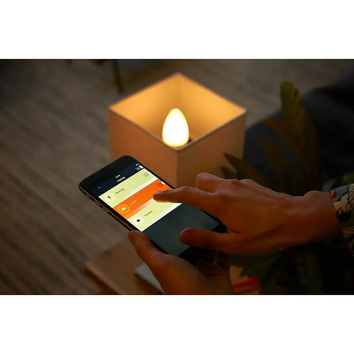Philips Hue Smart-LED-Lampen Set - E14, Dimmbar, RGBW, 470 lm, 5,3 W - Nahaufnahme einer Person, die eine App auf ihrem Smartphone bedient, um eine Hue Lampe zu steuern, die in einem quadratischen Gehäuse sitzt.