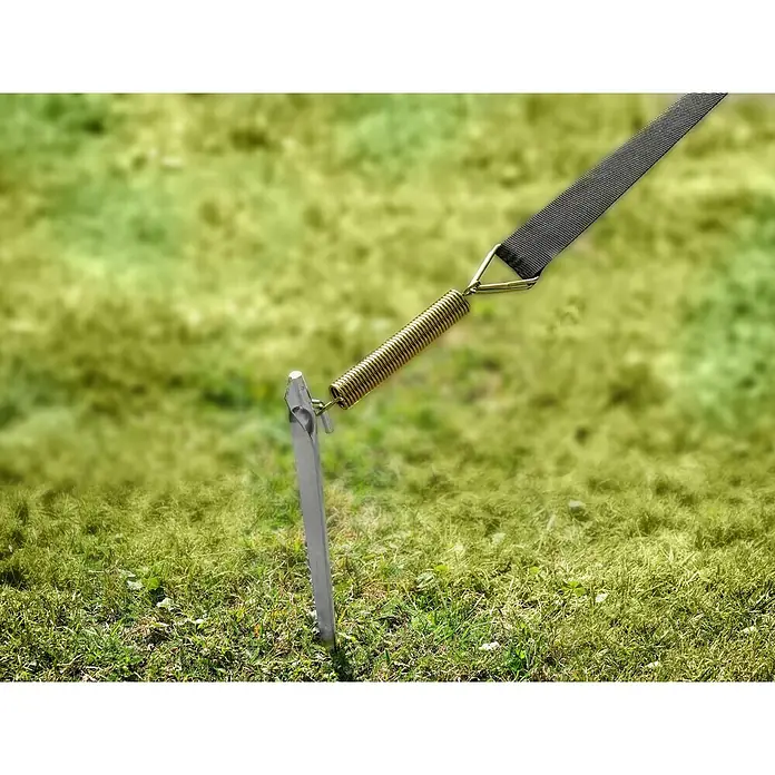 Abspann-Set - Zelte, 6 -tlg. - Nahaufnahme eines silbernen Zeltpflocks mit goldener Feder und schwarzem Gurt, der auf einer Wiese im Freien befestigt ist.